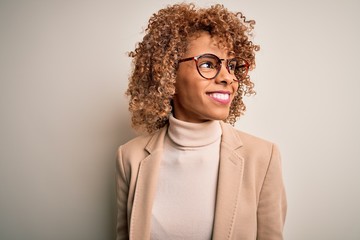 Beautiful african american businesswoman wearing glasses over isolated white background looking away to side with smile on face, natural expression. Laughing confident.