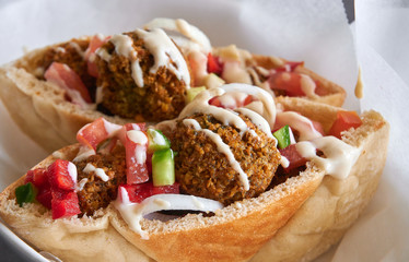 Authentic fresh falafels balls inside of two halves of pita bread sandwich with chopped salad and drizzle of tahini sauce on top, close-up of chickpea falafel in a gluten-free pita 