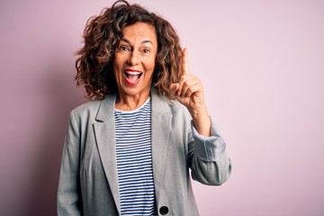 Sticker - Middle age beautiful businesswoman wearing elegant jacket over isolated pink background pointing finger up with successful idea. Exited and happy. Number one.