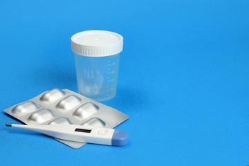 Urine container, tablets and thermometer on a blue background