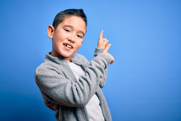 Canvas Print - Young little boy kid wearing sport sweatshirt over blue isolated background smiling and looking at the camera pointing with two hands and fingers to the side.