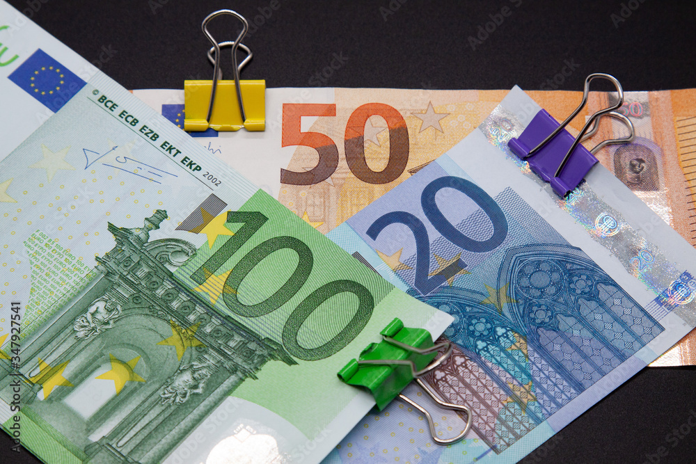Euro banknotes twelve, fifty, one hundred euros, colored paper clips on ...