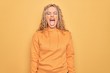 Young beautiful blonde sporty woman wearing casual sweatshirt over yellow background sticking tongue out happy with funny expression. Emotion concept.