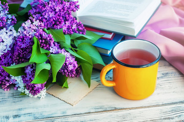 Wall Mural - Bouquet of a lilac, a yellow сup and books оn wooden background, selective focus.