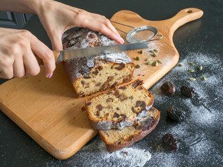 The cutting of the pieces of date cake. Homemade dates bread with walnuts on a black table