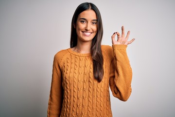 Young beautiful brunette woman wearing casual sweater over isolated white background smiling positive doing ok sign with hand and fingers. Successful expression.