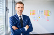 © baranq - Portrait of confident adult businessman standing at office with crossed arms, looking at camera