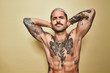 © Cien X Cien Studio/ADDICTIVE STOCK - Handsome sexy muscular male with various tattoos on naked torso and arms looking at camera while standing against beige background