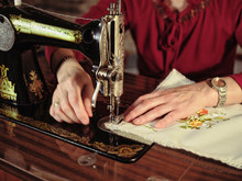 Senior Lady In Glasses Using Retro Sewing Machine To Create Linen Napkin In Cozy Room At Home