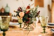 © Gustavo Pozo/ADDICTIVE STOCK - Bouquet of miscellaneous flowers and green plant twigs in vase with water on a wooden table set for a meal