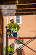 © Javier De La Torre/ADDICTIVE STOCK - Professional engineer in uniform and helmet sitting on scaffolding and looking away while working with colleague on maintenance of electric equipment near residential building