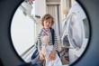 © PHILIPPE DEGROOTE/ADDICTIVE STOCK - Unhappy child in casual wear sitting on floor in front of washing machine with pile of dirty clothes around while doing housework at home
