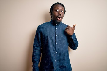 Wall Mural - Young handsome african american man wearing casual shirt standing over white background Surprised pointing with hand finger to the side, open mouth amazed expression.