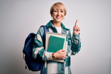 Sticker - Young blonde student woman with short hair wearing backpack and holding university books surprised with an idea or question pointing finger with happy face, number one