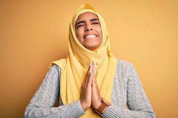 Sticker - Young beautiful african american girl wearing muslim hijab over isolated yellow background begging and praying with hands together with hope expression on face very emotional and worried. Begging.