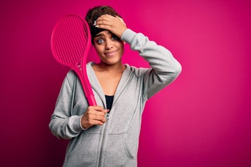 Canvas Print - Young african american sportswoman playing tennis using racket over isolated pink background stressed with hand on head, shocked with shame and surprise face, angry and frustrated. Fear and upset