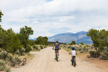 Rear View Of Mother And Son Riding Mountain Bikes On Desert Road