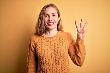 Sticker - Young beautiful blonde woman wearing casual sweater standing over yellow background showing and pointing up with fingers number three while smiling confident and happy.