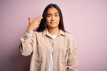 Young beautiful asian woman wearing casual shirt standing over pink background Shooting and killing oneself pointing hand and fingers to head like gun, suicide gesture.