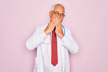 Wall Mural - Middle age senior grey-haired doctor man wearing stethoscope and professional medical coat laughing and embarrassed giggle covering mouth with hands, gossip and scandal concept