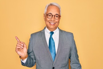 Canvas Print - Middle age senior grey-haired handsome business man wearing glasses over yellow background with a big smile on face, pointing with hand finger to the side looking at the camera.