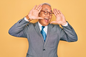 Sticker - Middle age senior grey-haired handsome business man wearing glasses over yellow background Smiling cheerful playing peek a boo with hands showing face. Surprised and exited