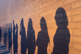 Fototapeta Dmuchawce - People crowd shadows lined up against a red brick wall. They are in a queue for changes in life. Social distance, covid and immigration issue concept