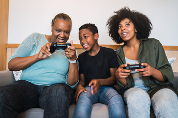 Grandmother, mother and son playing video games at home.