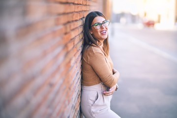 Wall Mural - Young beautiful woman smiling happy and confident. Standing with smile on face leaning on the wall at the town street