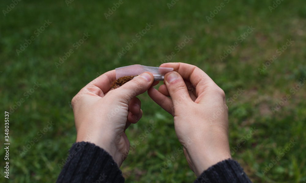 roll a cigarette with one hand First person hands rolling a tobacco cigarette. POV. Stock Photo