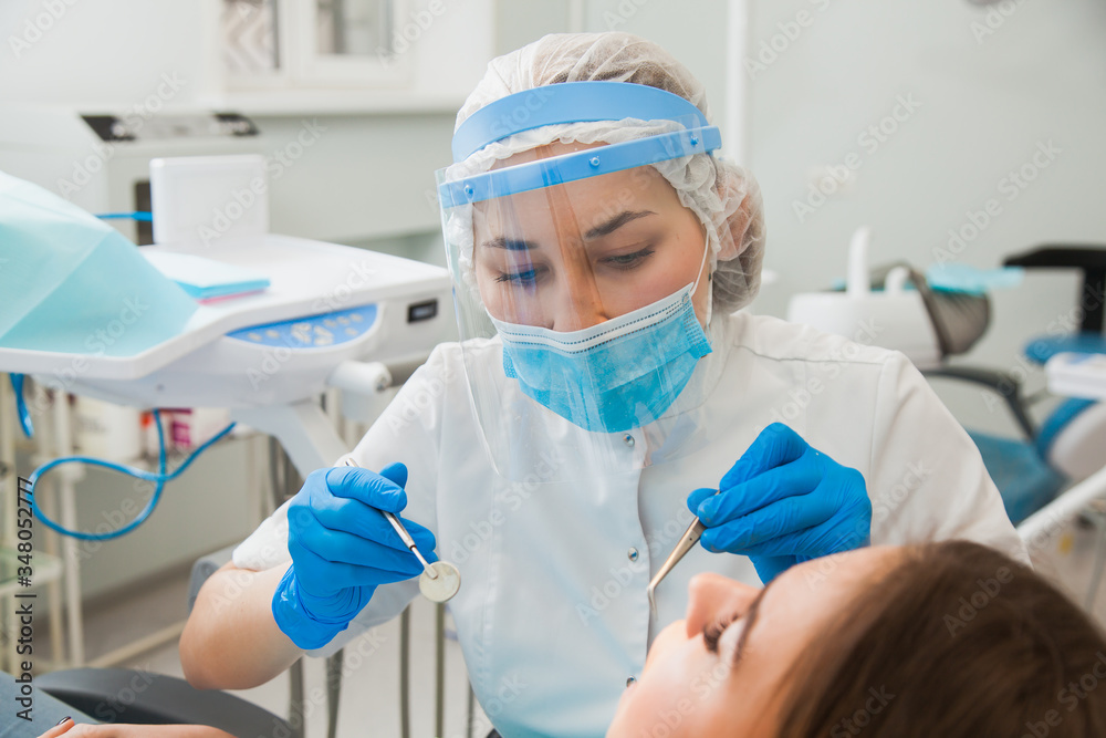 Young female dentist curing patient's teeth filling cavity - obrazy, fototapety, plakaty 