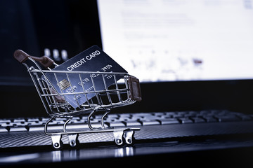 Poster - close up Shallow focus Credit Card in mini shopping card with Computer keyboard and E-commerce website on monitor background. Background for E-commerce and online shopping concept.