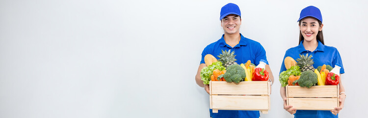 Closeup portrait of asian couple delivery man woman in blue uniform hold fresh grocery vegetables food isolated on white. Healthy lifestyle shopping internet online supermarket delivery teamwork