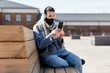 © Syda Productions - health, safety and pandemic concept - young woman wearing protective medical mask and using smartphone on city street