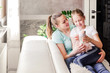 © ribalka yuli - Mother with her adult daughter sitting together and having good time in the living room in front of window. Daughter shows mom a doll. Horizontal photo