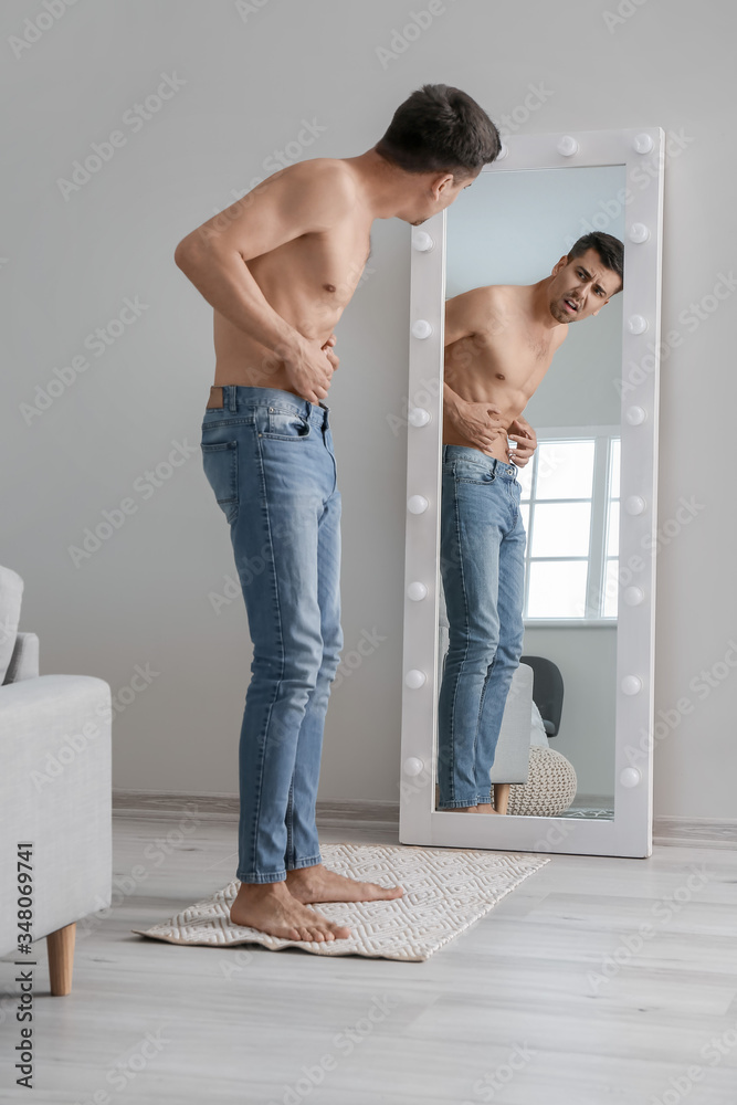 Young man with anorexia looking on his reflection in mirror at home