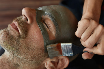 Wall Mural - Spa Face Mask. Beauty Treatment For Skin Care. Beautician Applying Mud On Man's Face. Relaxed Model On Natural Cosmetic Procedure.