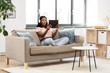 © Syda Productions - people, technology and leisure concept - surprised young african american woman with tablet pc computer and headphones sitting on sofa and listening to music at home