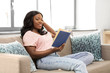 © Syda Productions - people and leisure concept - happy smiling african american woman sitting on sofa and reading book at home