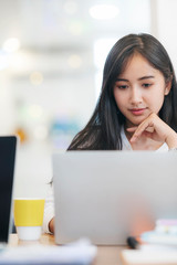 Young asian woman with hand  touching her chin working with laptop.