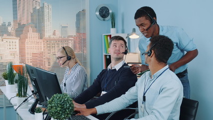 Wall Mural - Multiethnic customer service representative telling his colleagues a joke while calling to the clients. They laughing and continuing working.