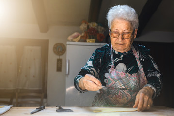 Caucasian old woman cooking in her kitchen traditional recipes of Italian cuisine. Throwing flour on the dough to prepare fresh homemade pasta.