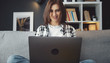 © MYDAYcontent - Front view of young smiling lady sitting on sofa holding laptop on her lap and looking at screen