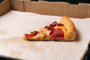 Wall Mural - Closeup of the last whole slice of pepperoni pizza in a cardboard paper box on a dark background