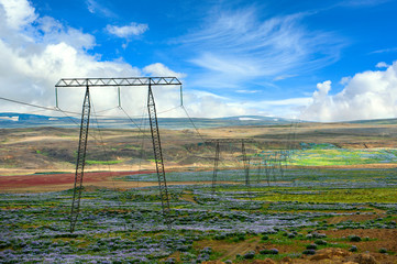 Sticker - High-voltage electricity poles and power lines in the midst of nature in Iceland. In the summer, purple lupine blooms all over the place. On a clear blue sky and beautiful clouds.