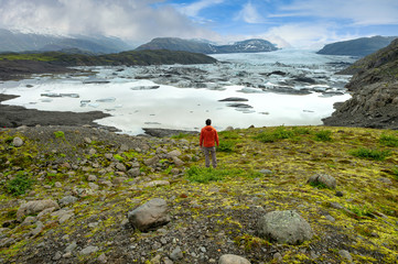 Canvas Print - oung man wearing a red shirt stands looking at a large glacier at the Skaftafell lagoon in southern Iceland, the great nature of Gracier in the summer on a bright blue sky.