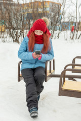 Portrait of young beautiful woman in red hat and red comforter sitting on the carousel and calling phone