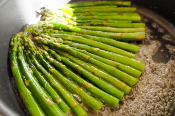 green asparagus stalks are fried in a large pan with the liquid evaporating . caramelization of asparagus with sugar, salt, water and butter . gluten-free diet