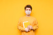 © bodnarphoto - Upset student in a medical mask stands on a yellow background with books and notebooks in his hands and looks into the camera with a sad face. Quarantine training. Student in quarantine.