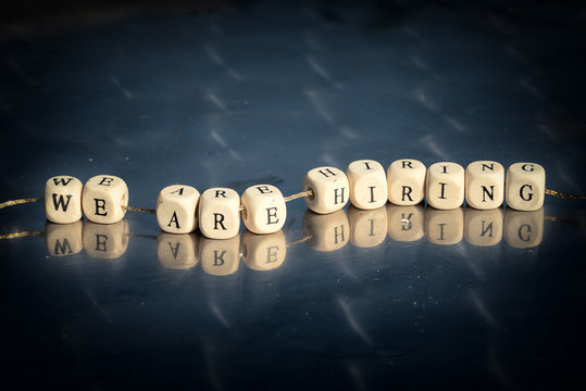 Wooden cubes with we are hiring inscription strung on a thread on reflective table. The recruitment business concept.